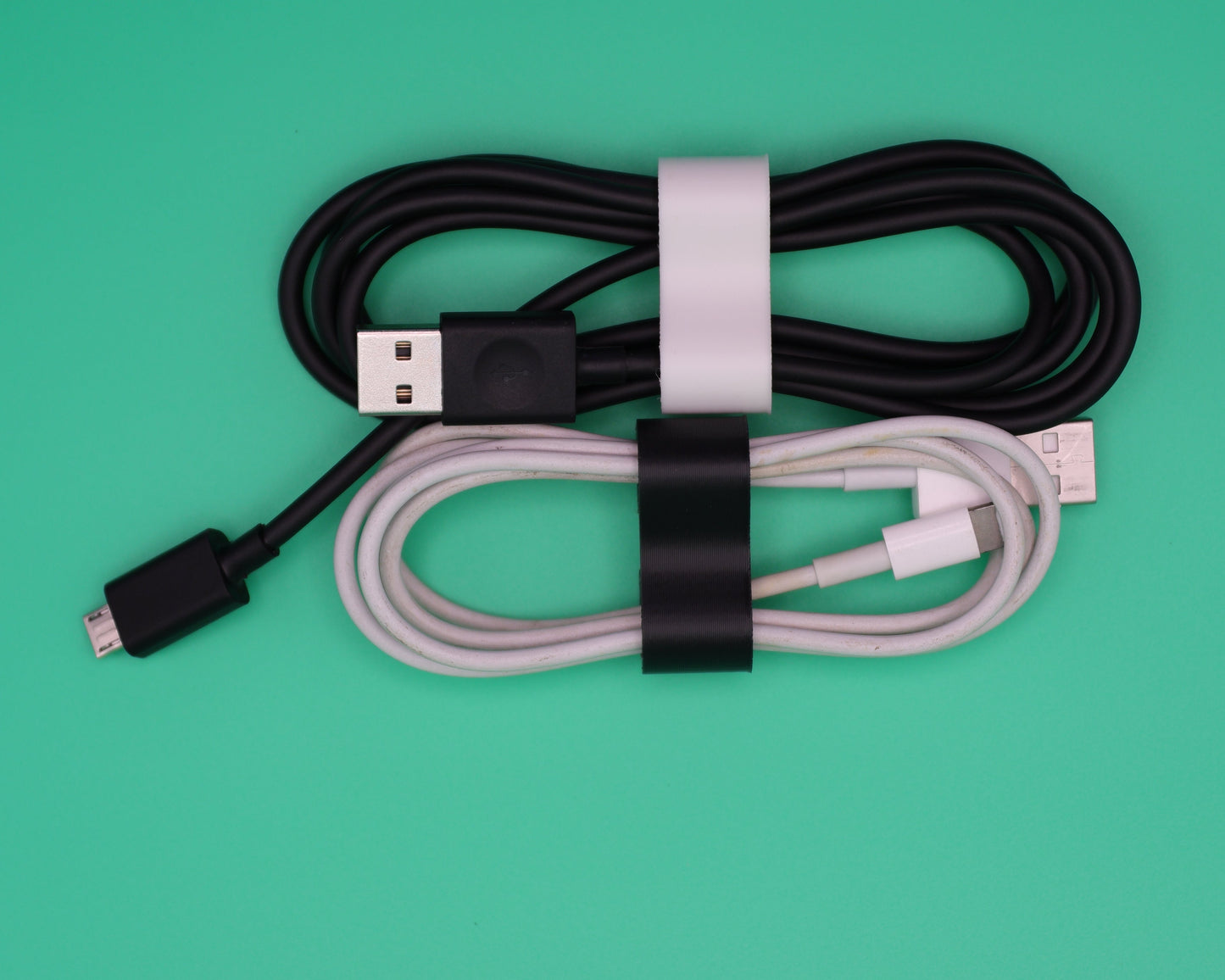 Close-up of a DualForge3D ForgeWrap compact cord keeper in matte black holding a white USB-C charging cable neatly wound