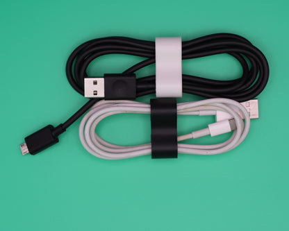Close-up of a DualForge3D ForgeWrap compact cord keeper in matte black holding a white USB-C charging cable neatly wound